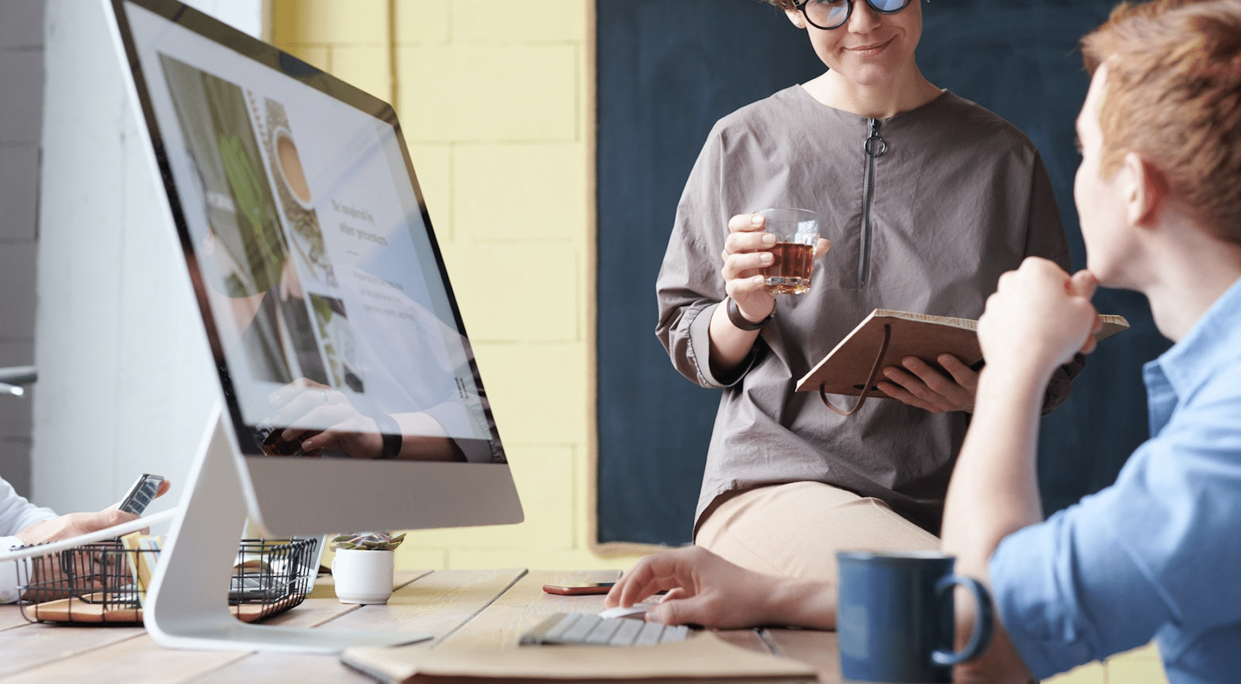 Medarbejdere i dialog foran stor computerskærm på kontor, illustrerer behov for skærmbriller og ergonomiske brilleløsninger til virksomheder