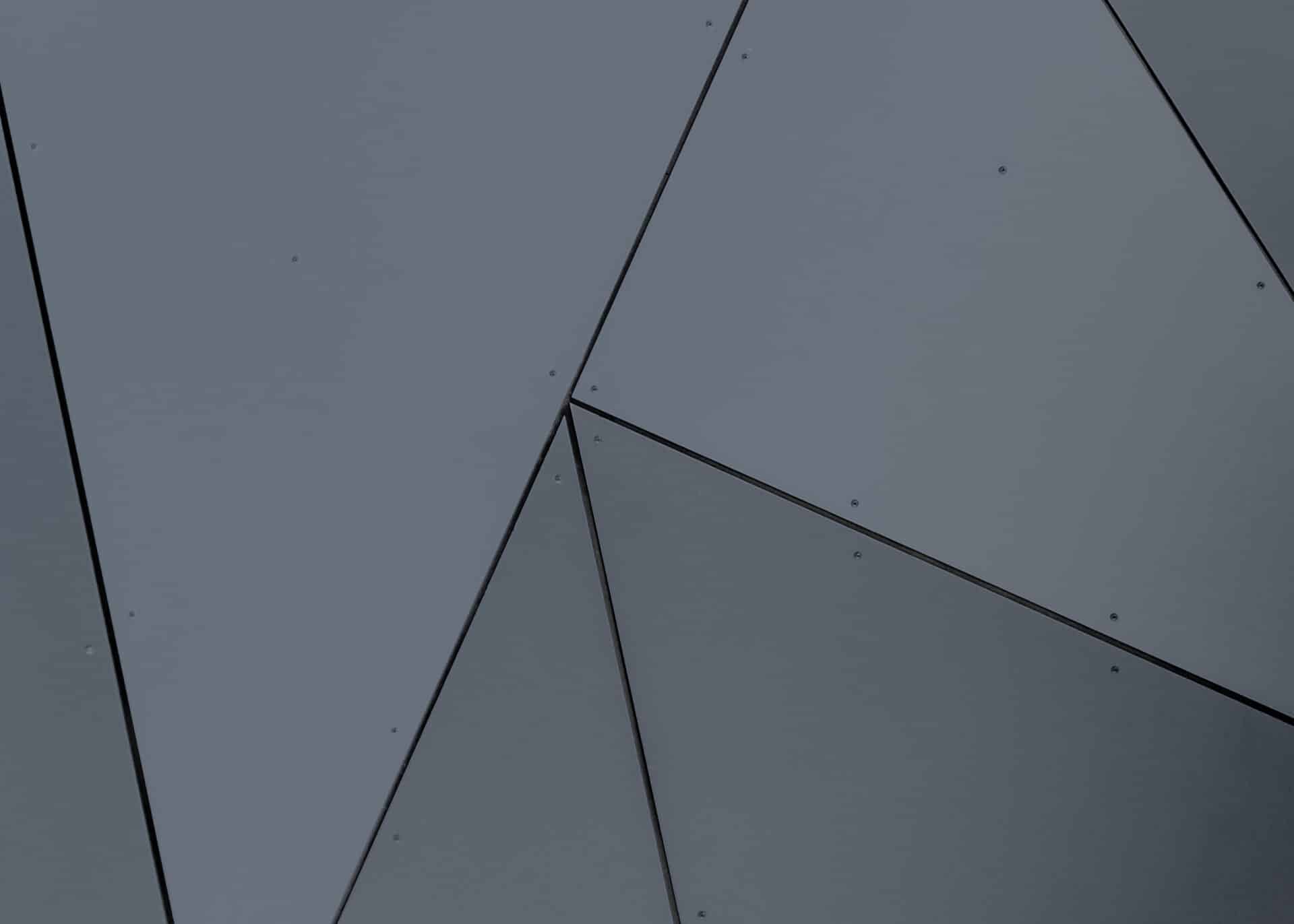 Grå væg med geometrisk mønster, anvendt som baggrundsbillede i relation til Dansk Erhvervsoptik og visuel identitet for erhvervsoptik løsninger